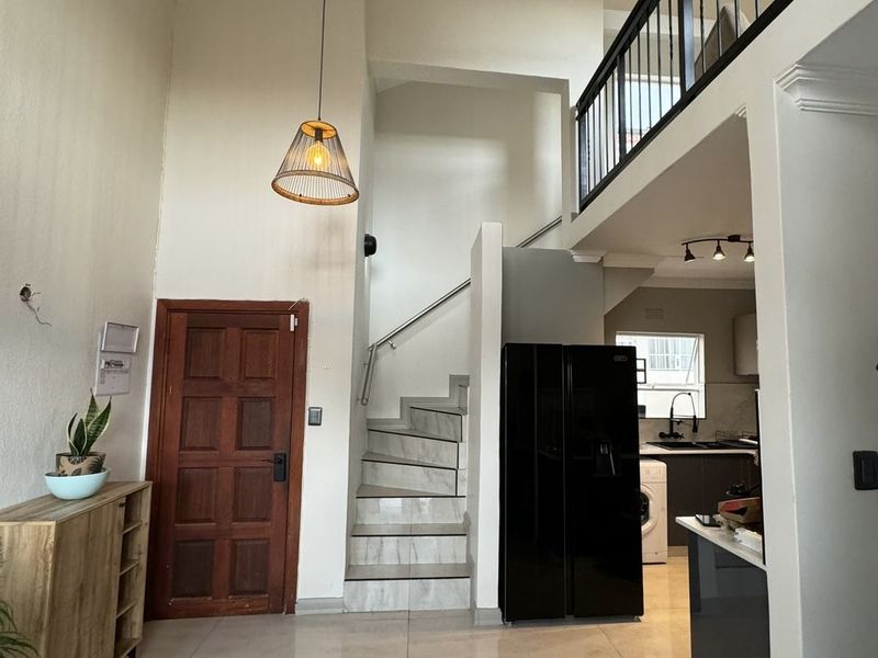 Open plan living area featuring a double-volume ceiling, a modern staircase with metal balustrades, and a mezzanine level overlooking the kitchen and entrance.
