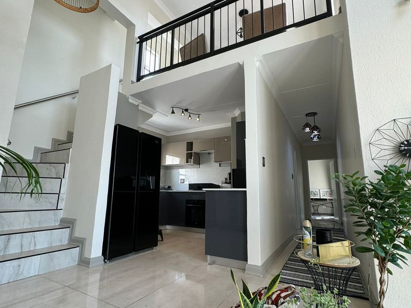 Spacious open-plan living area featuring a modern kitchen, tiled floors, and a staircase leading to a mezzanine level with a metal balustrade.