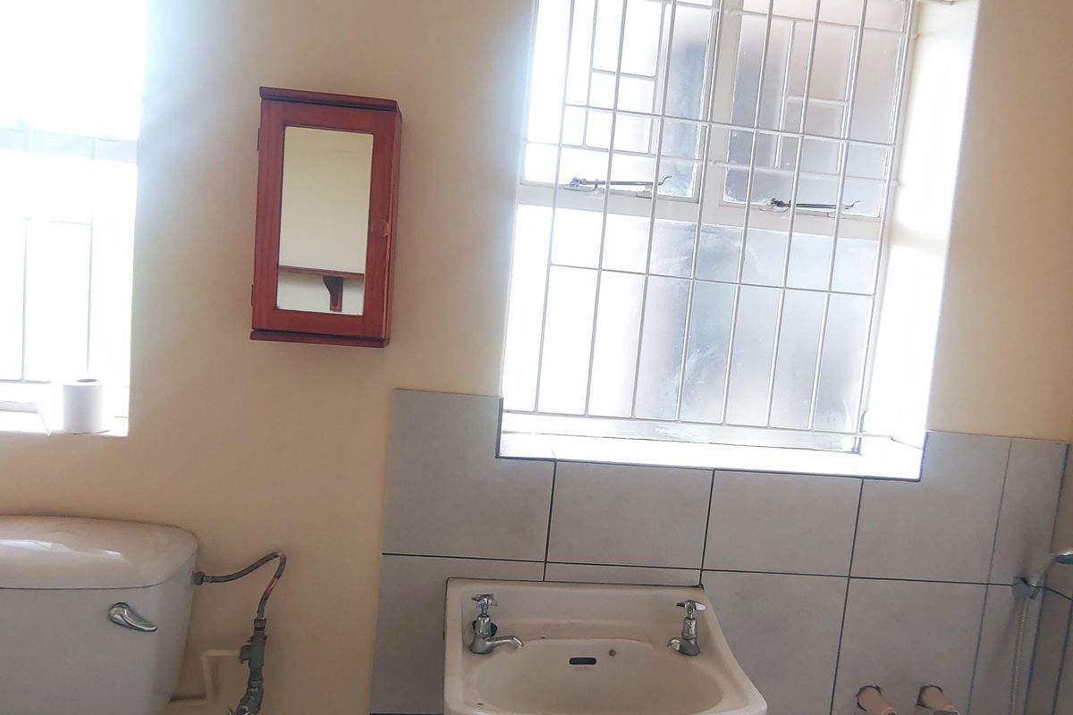 A functional bathroom featuring a wall-mounted basin, bathtub with shower mixer, and toilet, finished with neutral wall tiles and security bars on windows.