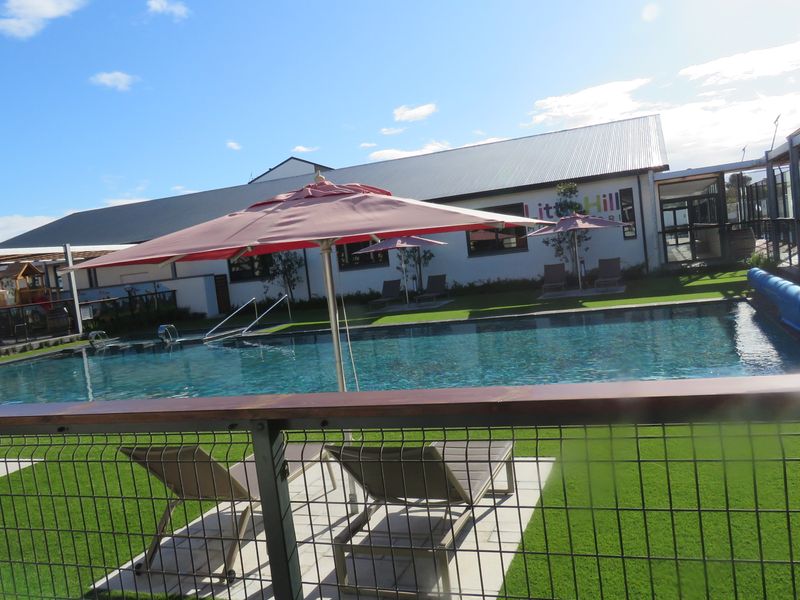 A well-maintained outdoor swimming pool area featuring artificial turf, paved decking, and secure metal mesh fencing.