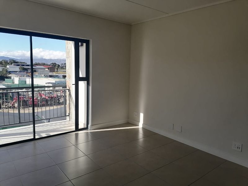 A bright, empty living area featuring neutral tiled flooring and a large sliding glass door providing access to a private balcony.