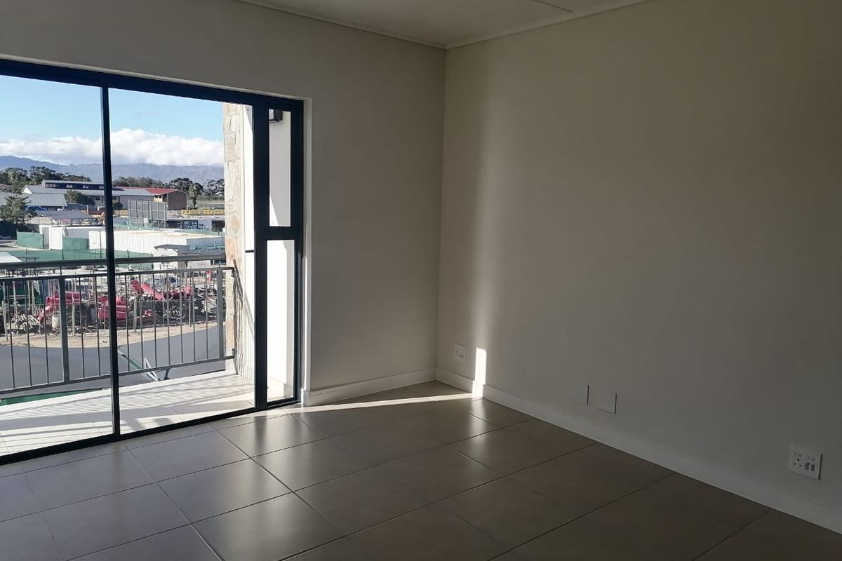 A bright, empty living area featuring neutral tiled flooring and a large sliding glass door providing access to a private balcony.