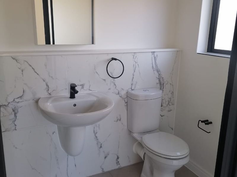 A modern, clean bathroom featuring marble-look wall tiling, a wall-mounted basin with black tapware, and a standard toilet.