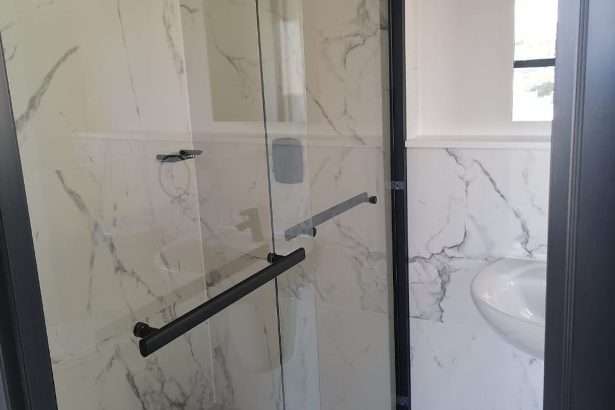 A modern bathroom featuring a walk-in shower with a black frame, marble-look wall tiles, and a wall-mounted basin.