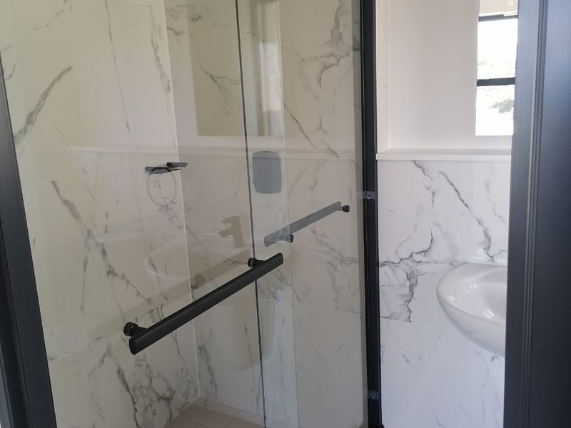 A modern bathroom featuring a walk-in shower with a black frame, marble-look wall tiles, and a wall-mounted basin.