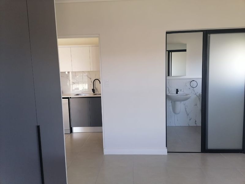 Modern open-plan apartment interior featuring a sleek kitchen with marble-look splashback and a contemporary bathroom with pedestal basin and black fixtures.