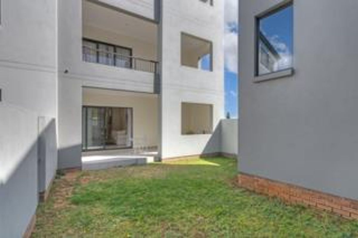 A view of the rear exterior of the apartment building, featuring a private garden area and covered patio access.