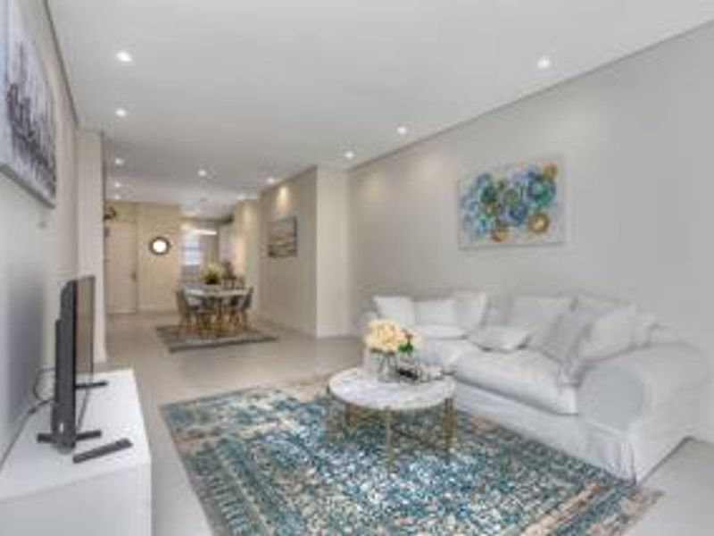 An open-plan living and dining area featuring neutral tiled flooring, recessed downlighting, and a clean, modern aesthetic.