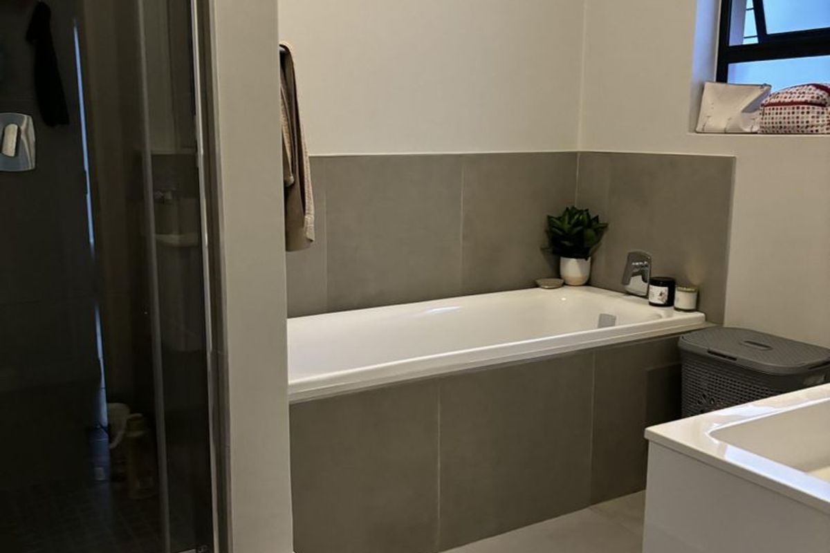Modern bathroom featuring a built-in bathtub with neutral tiling, a separate glass-enclosed shower, and a window for natural light.
