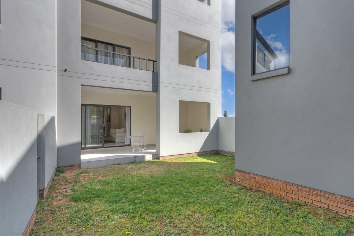 A view of the apartment's rear exterior, featuring a private patio area, a small garden space, and modern multi-story building architecture.