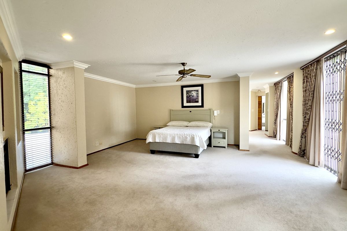 Spacious bedroom featuring neutral carpeting, a ceiling fan, and large windows with security gates, offering a bright and comfortable living space.