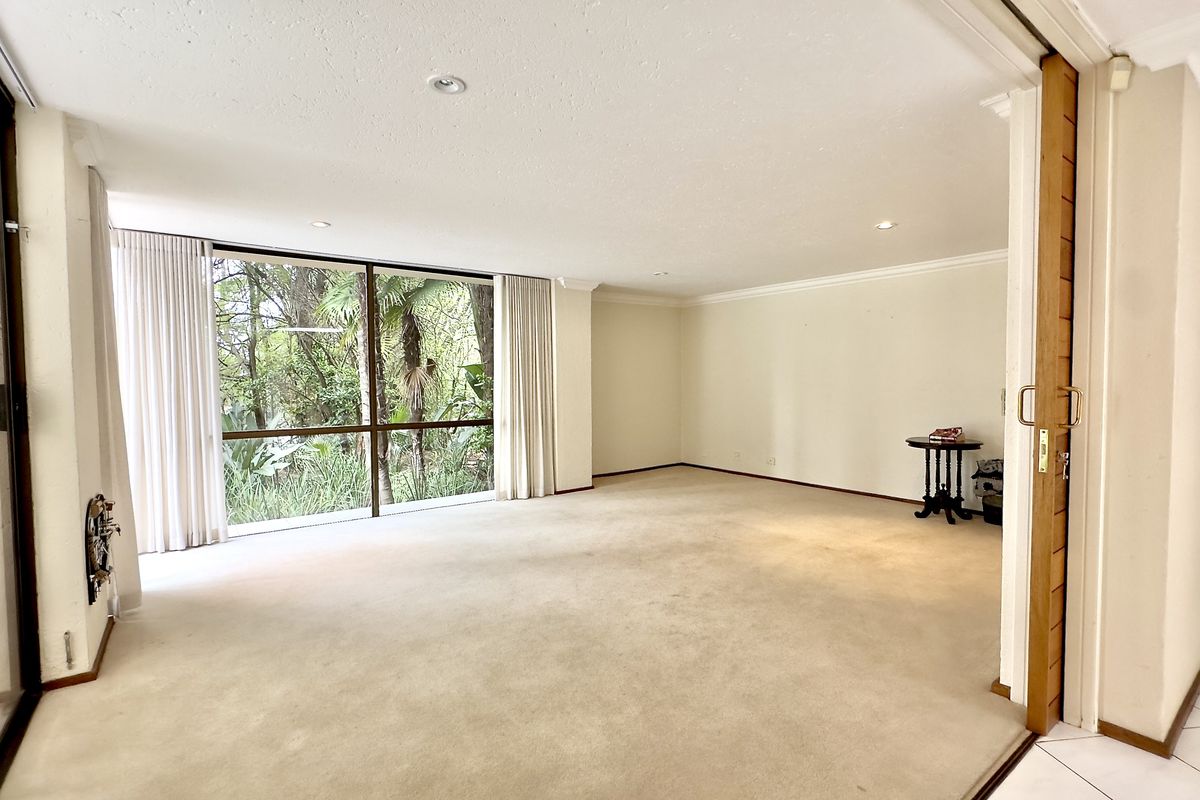 Spacious living area featuring large floor-to-ceiling windows with garden views, neutral carpeting, and sliding door access to the exterior.