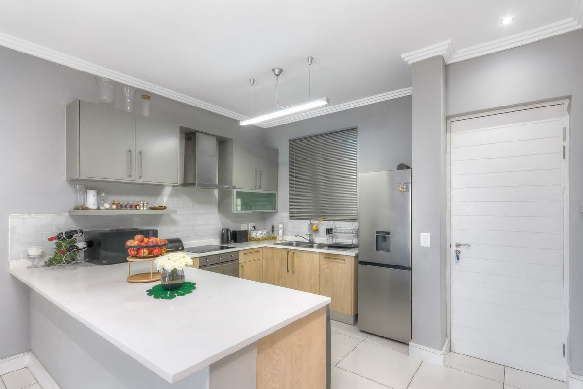 Modern kitchen featuring light wood cabinetry, white stone countertops, subway tile backsplash, integrated hob, and stainless steel extractor fan.