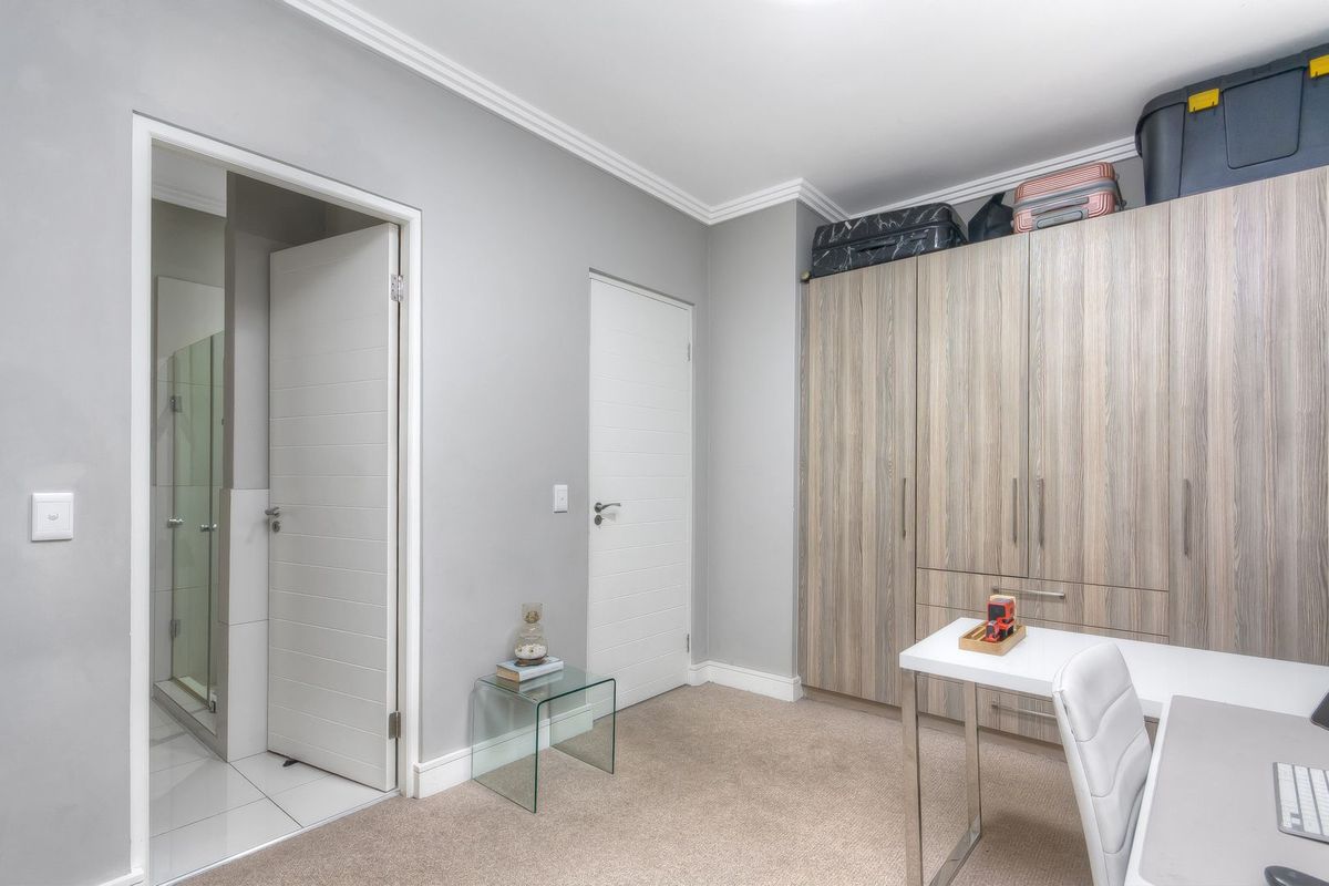 A bedroom featuring built-in wooden cabinetry, neutral carpeting, crown molding, and an en-suite bathroom entrance.