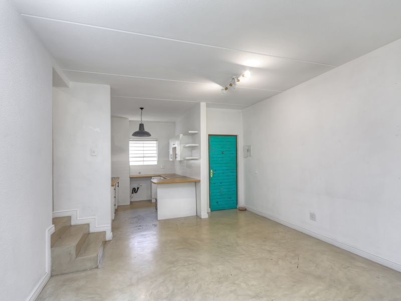An open-plan living and kitchen area featuring a staircase, concrete flooring, and basic kitchen cabinetry in a vacant apartment setting.