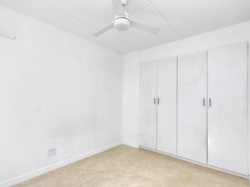 A vacant bedroom featuring built-in cupboards, a ceiling fan, and neutral flooring, offering a blank canvas for personalization.