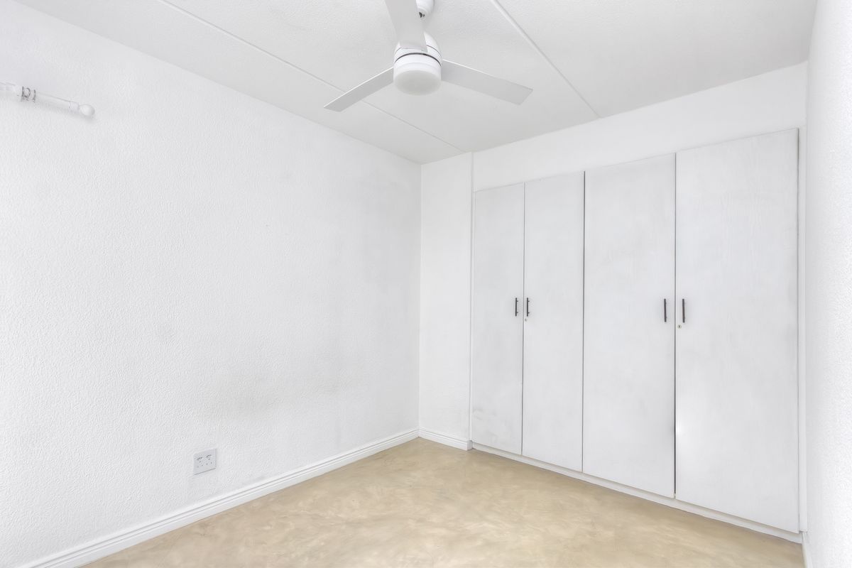 A vacant bedroom featuring built-in cupboards, a ceiling fan, and neutral flooring, offering a blank canvas for personalization.