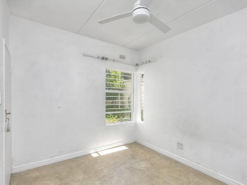 An empty bedroom featuring a ceiling fan, concrete flooring, and a window with security bars, ready for personalization.