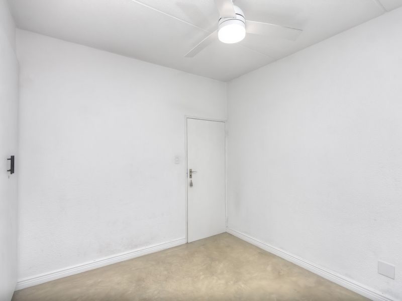 A clean, empty bedroom featuring a ceiling fan, neutral wall finishes, and polished concrete flooring, ready for personalization.