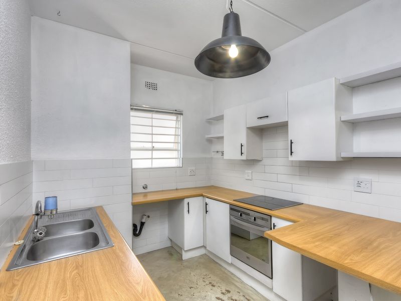 A clean, functional kitchen featuring white cabinetry, wooden countertops, a built-in oven, electric hob, and a double bowl stainless steel sink.
