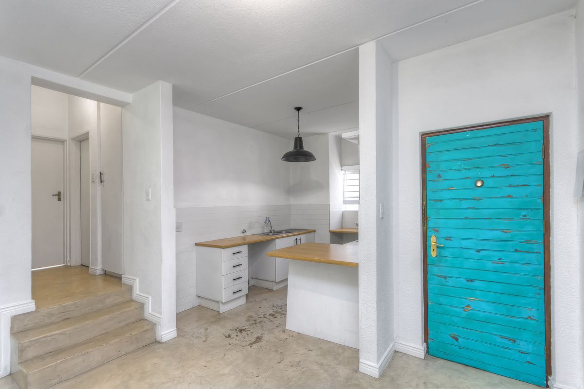 An empty kitchen area featuring wooden countertops, built-in cabinetry, and a tiled backsplash, adjacent to an internal staircase and a distinctive turquoise door.