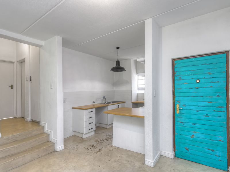An empty kitchen area featuring wooden countertops, built-in cabinetry, and a tiled backsplash, adjacent to an internal staircase and a distinctive turquoise door.