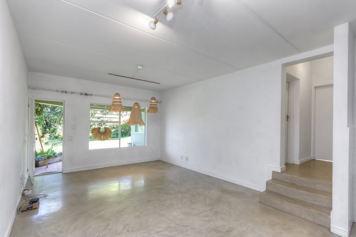 An open-plan living area featuring polished concrete floors, neutral walls, and direct access to an outdoor garden space via a side door.