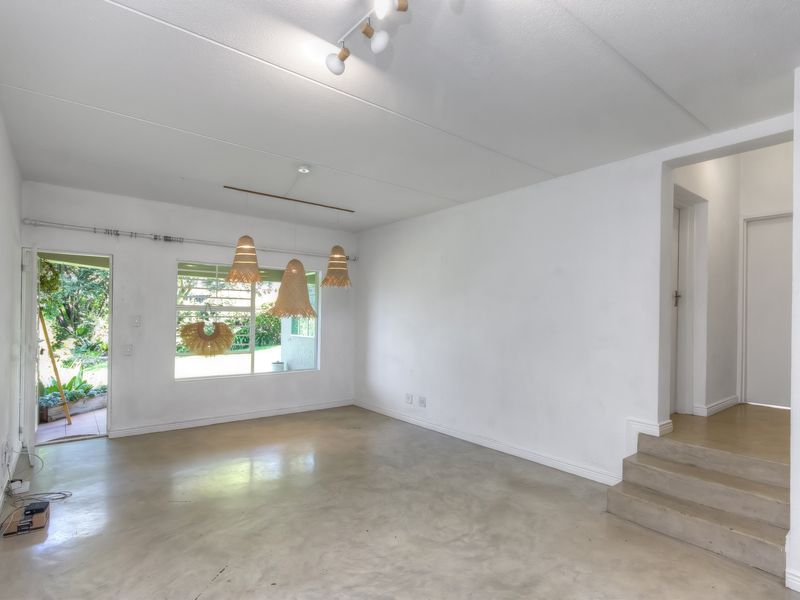 An open-plan living area featuring polished concrete floors, neutral walls, and direct access to an outdoor garden space via a side door.