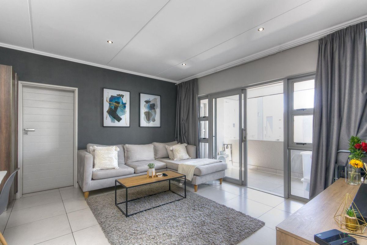 A modern living room featuring tiled flooring, recessed ceiling lighting, and large sliding glass doors that open onto a private balcony.