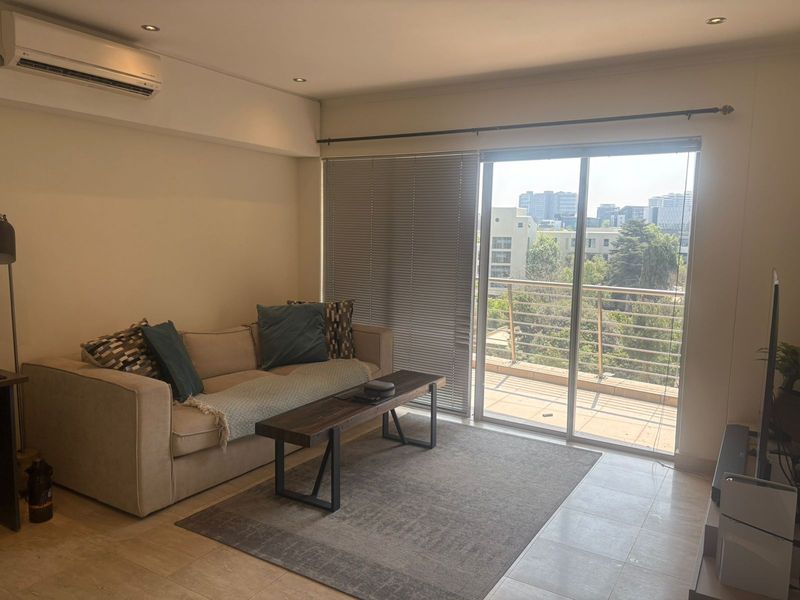A bright living room featuring tiled floors, recessed lighting, and a split-system air conditioner, with direct access to a balcony through sliding glass doors.