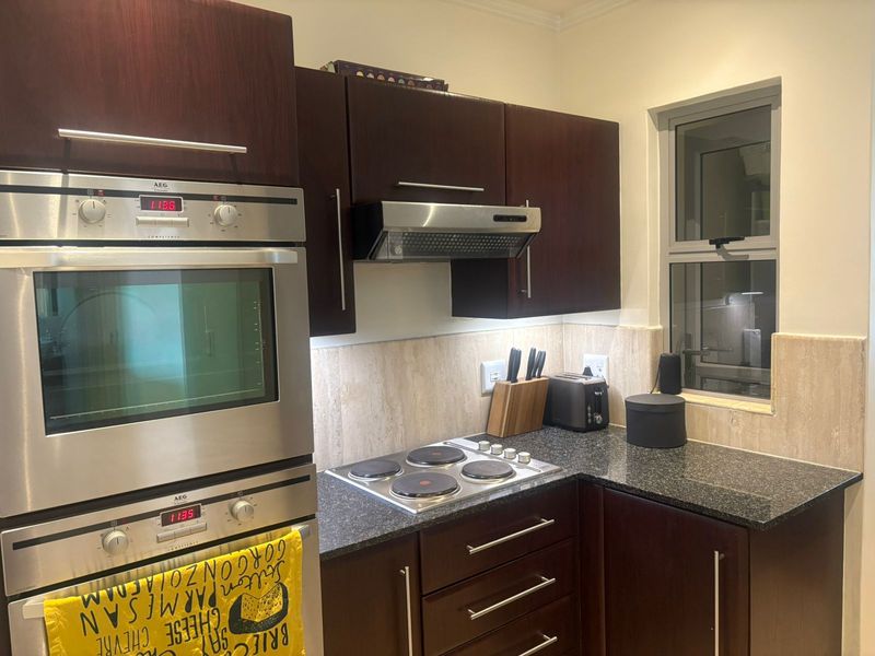 A compact kitchen featuring dark wood cabinetry, granite countertops, a built-in AEG oven, and an electric hob with an integrated extractor fan.
