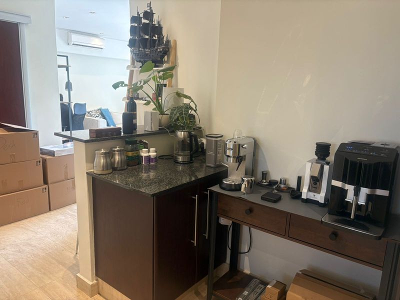 A compact kitchen area featuring dark wood cabinetry, granite countertops, and recessed lighting, with an adjacent living space visible in the background.