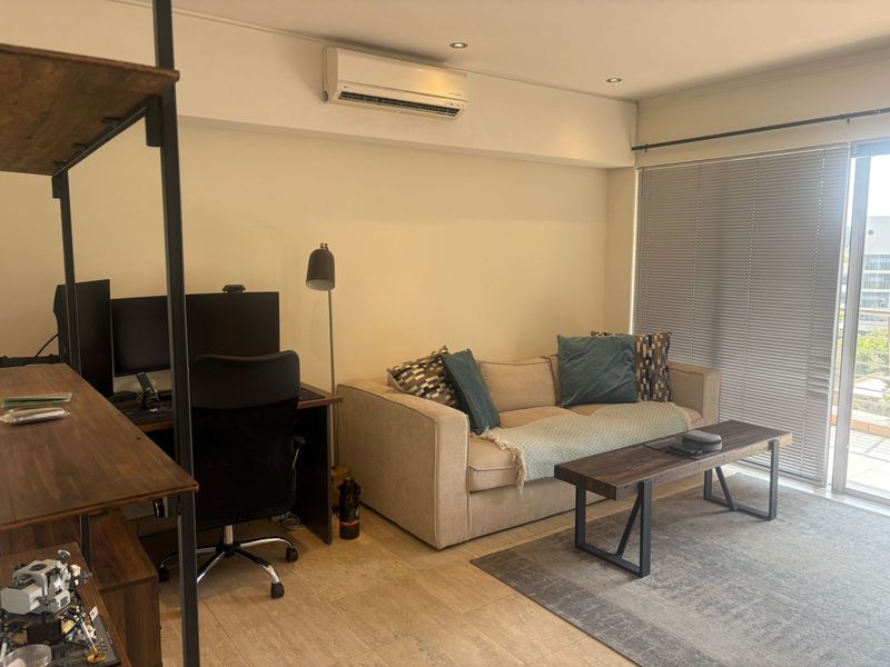 A well-maintained living area featuring tiled flooring, recessed lighting, a wall-mounted air conditioning unit, and large sliding glass doors with venetian blinds.