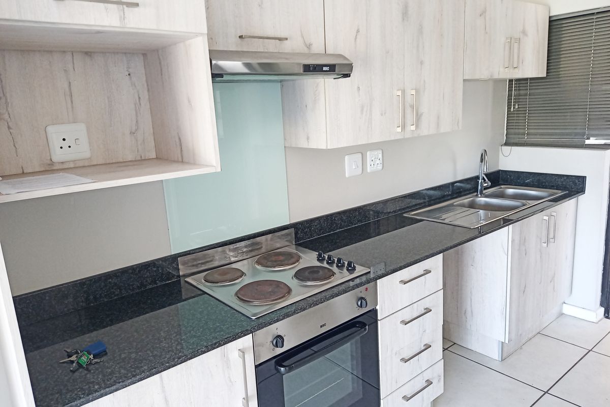 Modern kitchen featuring light wood-grain cabinetry, dark granite countertops, built-in electric oven and hob, extractor fan, and a double sink with mixer tap.