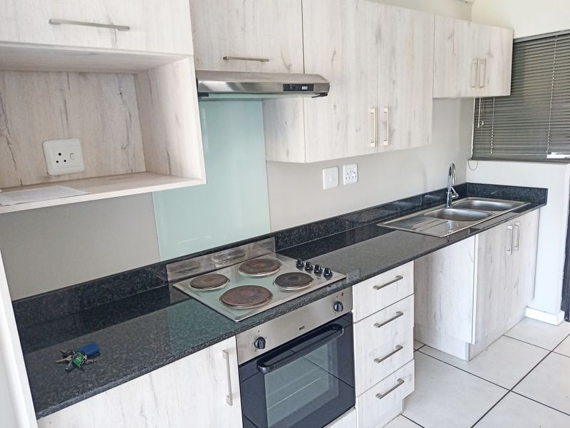 Modern kitchen featuring light wood-grain cabinetry, dark granite countertops, built-in electric oven and hob, extractor fan, and a double sink with mixer tap.