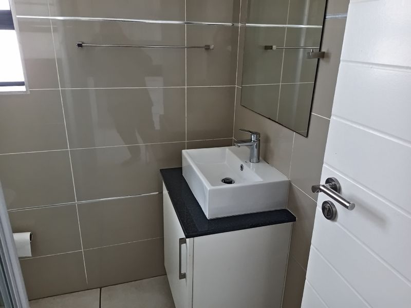 A modern bathroom featuring a white vessel sink on a dark countertop, vanity cabinet, wall mirror, and neutral tiled walls.