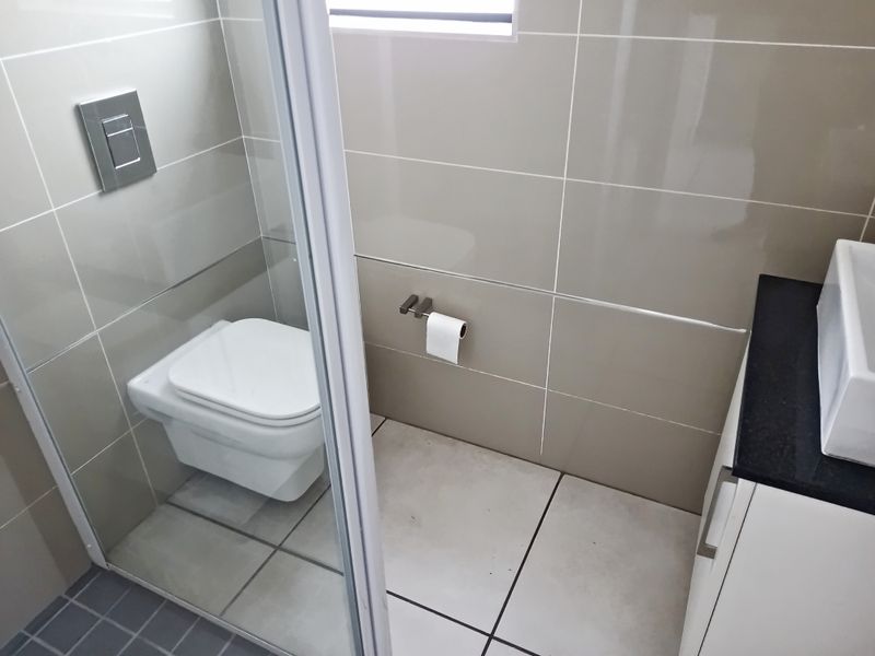 A modern bathroom featuring a wall-mounted toilet with a flush plate, a vanity cabinet with a countertop basin, and neutral ceramic tiling.