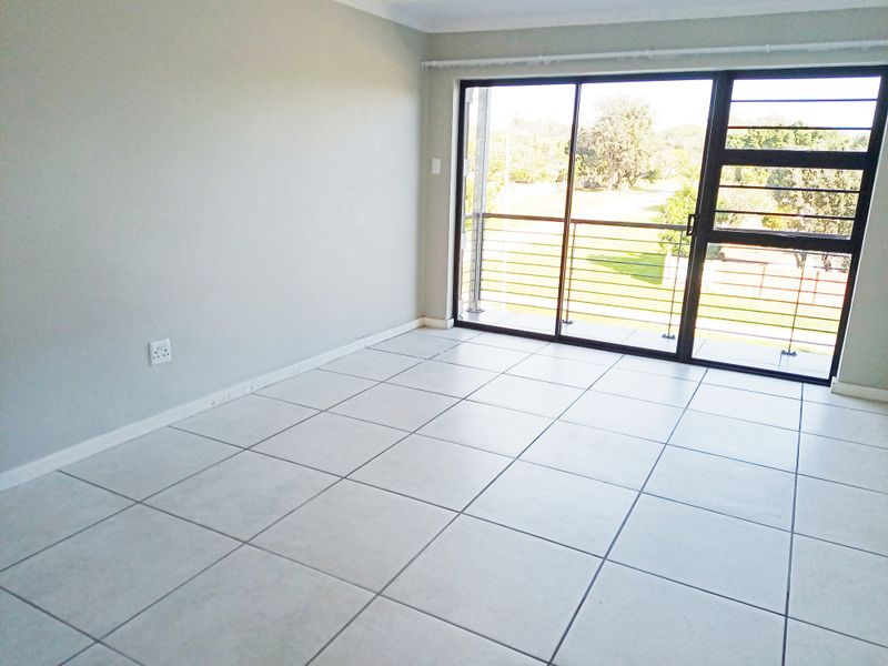 An empty living room featuring neutral ceramic floor tiles, large sliding glass doors with security bars, and access to an outdoor balcony area.
