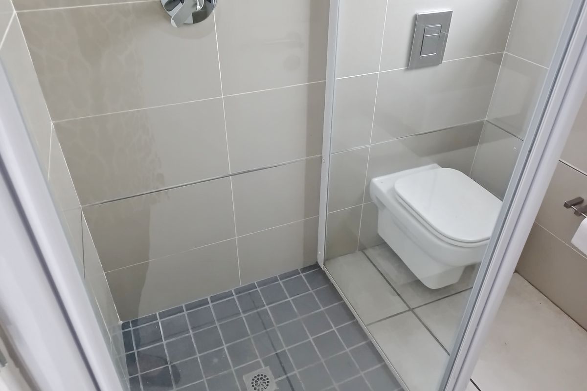 A modern bathroom featuring a wall-mounted toilet with a concealed cistern and a tiled shower enclosure with a glass screen.