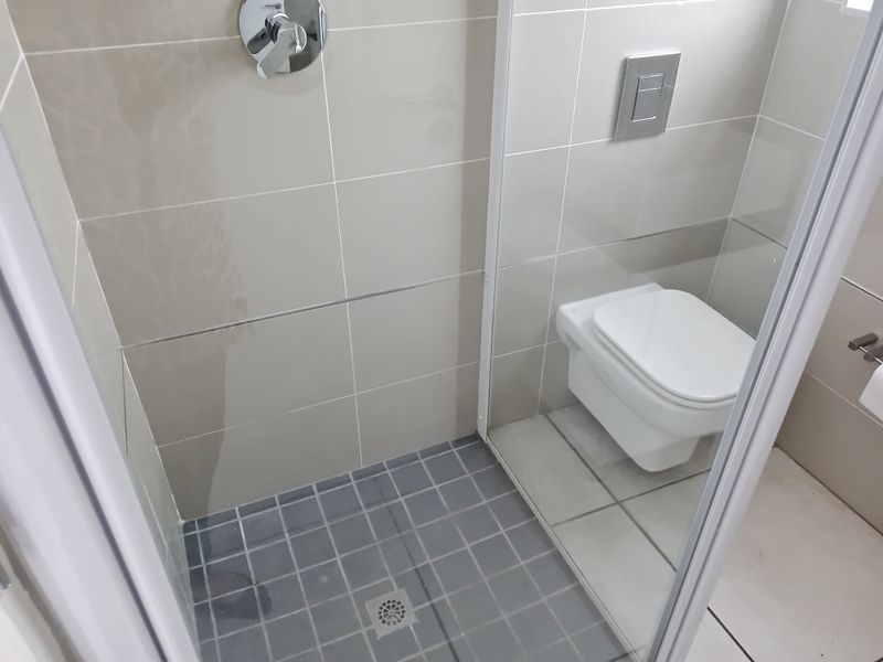 A modern bathroom featuring a wall-mounted toilet with a concealed cistern and a tiled shower enclosure with a glass screen.