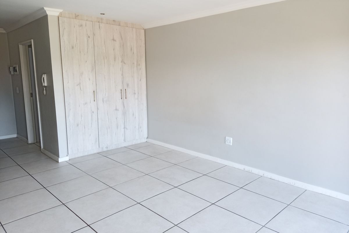 A bright, empty living area featuring neutral tiled flooring, built-in storage cupboards, and recessed downlighting, providing a clean and versatile space.