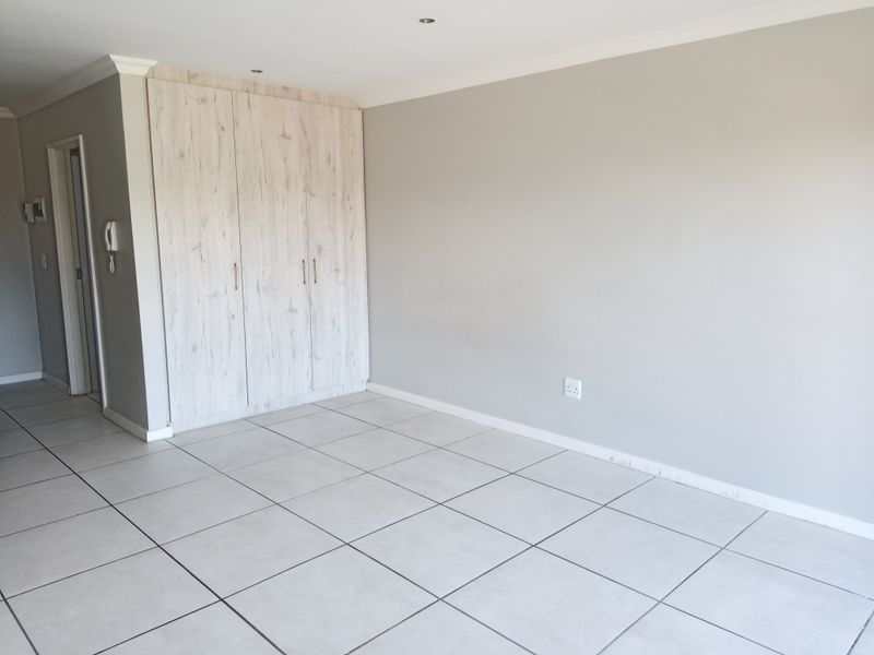 A bright, empty living area featuring neutral tiled flooring, built-in storage cupboards, and recessed downlighting, providing a clean and versatile space.