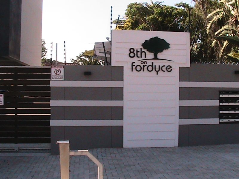 The front entrance of the 8th on Fordyce apartment complex, featuring a secure boundary wall, electric fencing, and a gated access point.