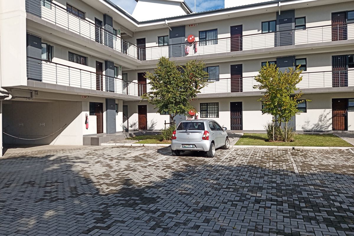Exterior view of a modern apartment complex featuring paved parking, multi-level balconies with metal railings, and well-maintained communal grounds.