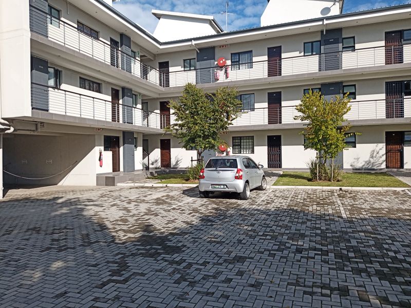 Exterior view of a modern apartment complex featuring paved parking, multi-level balconies with metal railings, and well-maintained communal grounds.