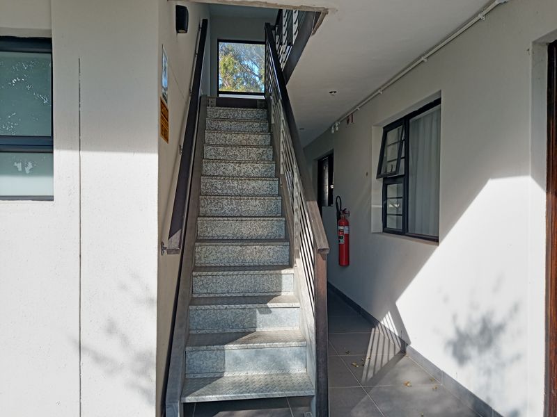Exterior stairwell entrance featuring metal stairs, tiled flooring, and a wall-mounted fire extinguisher in an apartment complex.