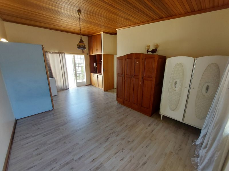 Spacious bedroom featuring timber ceiling, laminate flooring, and built-in storage, with direct access to an outdoor area through a glass panel door.
