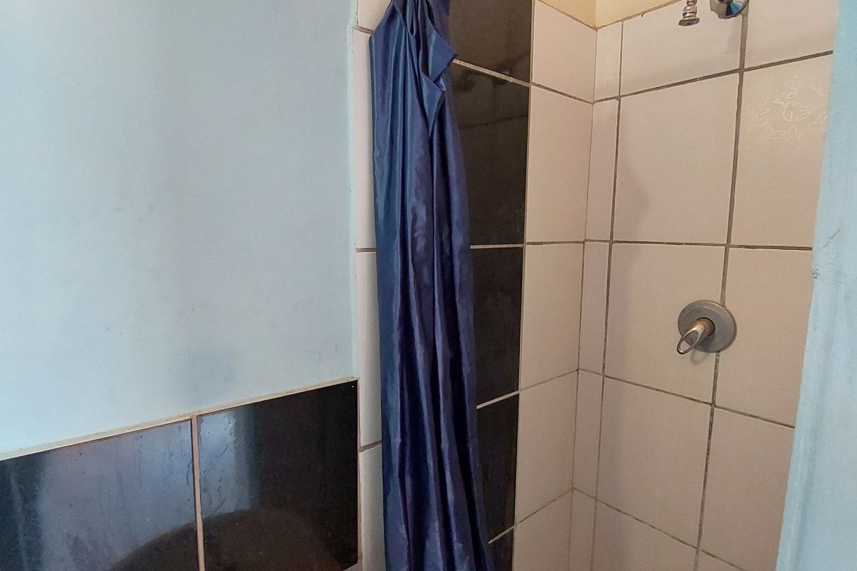 A compact bathroom featuring a wall-mounted basin and a shower area with tiled finishes, requiring some maintenance and cosmetic updates.