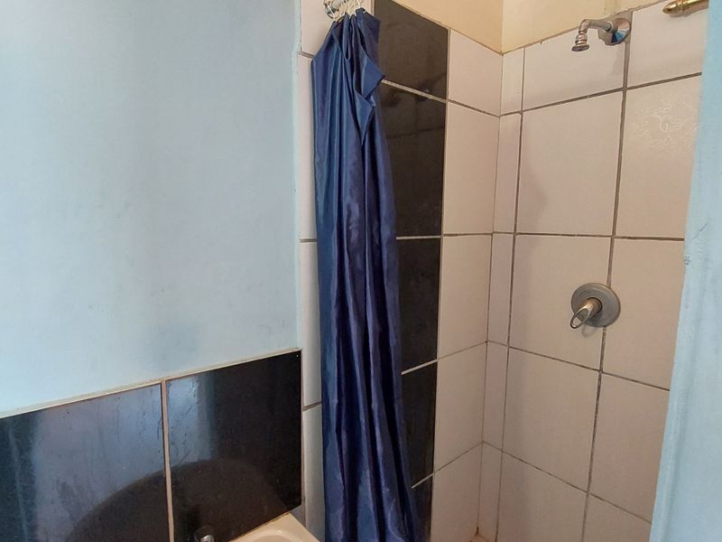 A compact bathroom featuring a wall-mounted basin and a shower area with tiled finishes, requiring some maintenance and cosmetic updates.