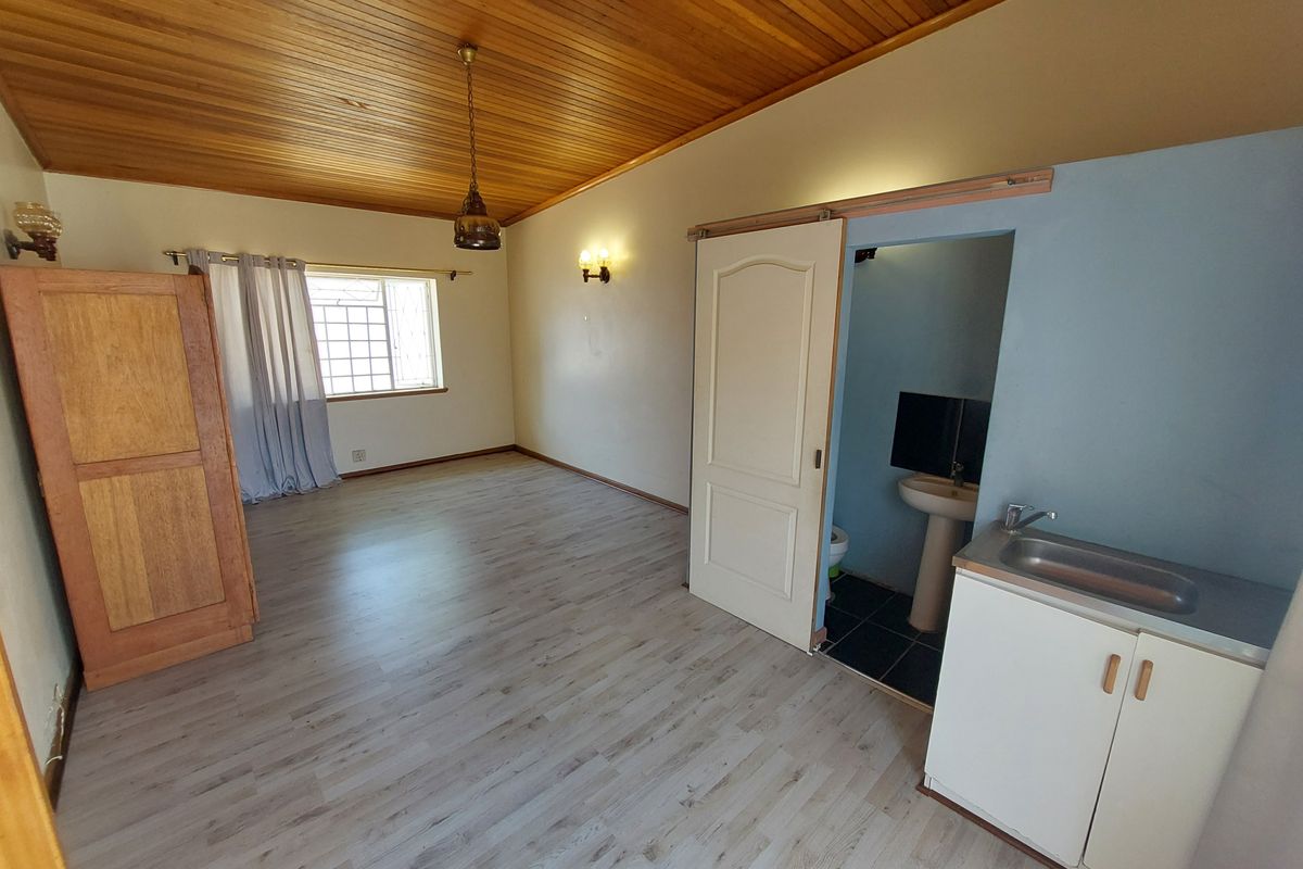 A bedroom featuring a timber ceiling, laminate flooring, and an en-suite bathroom with a pedestal basin and vanity cabinet.